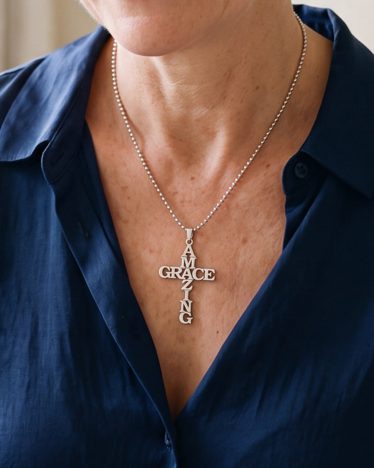 The Amazing Grace cross worn by a woman, close-up from chin to chest, true to size