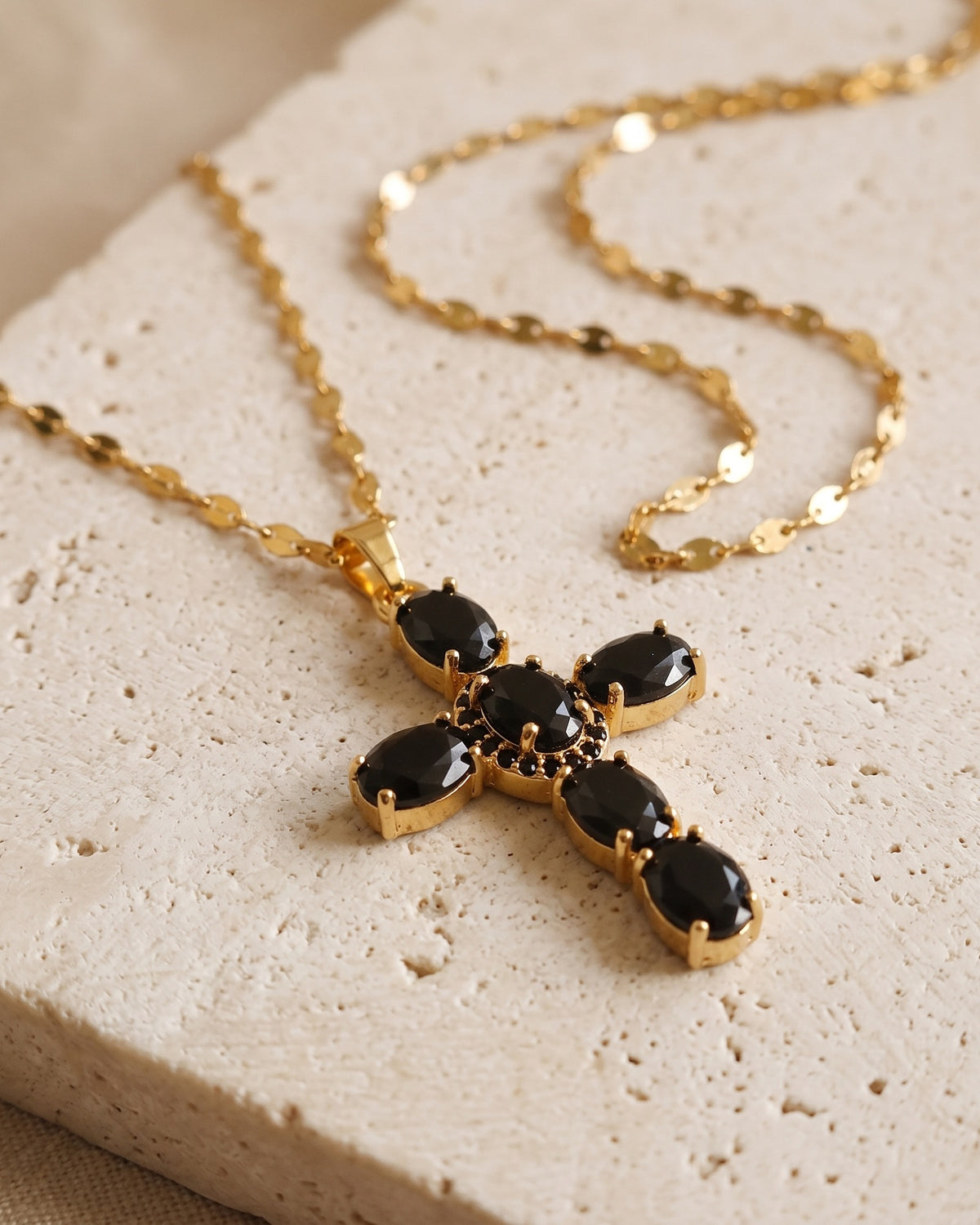 The gold Obsidian Cross with black stones on stone, side view [c:gold]