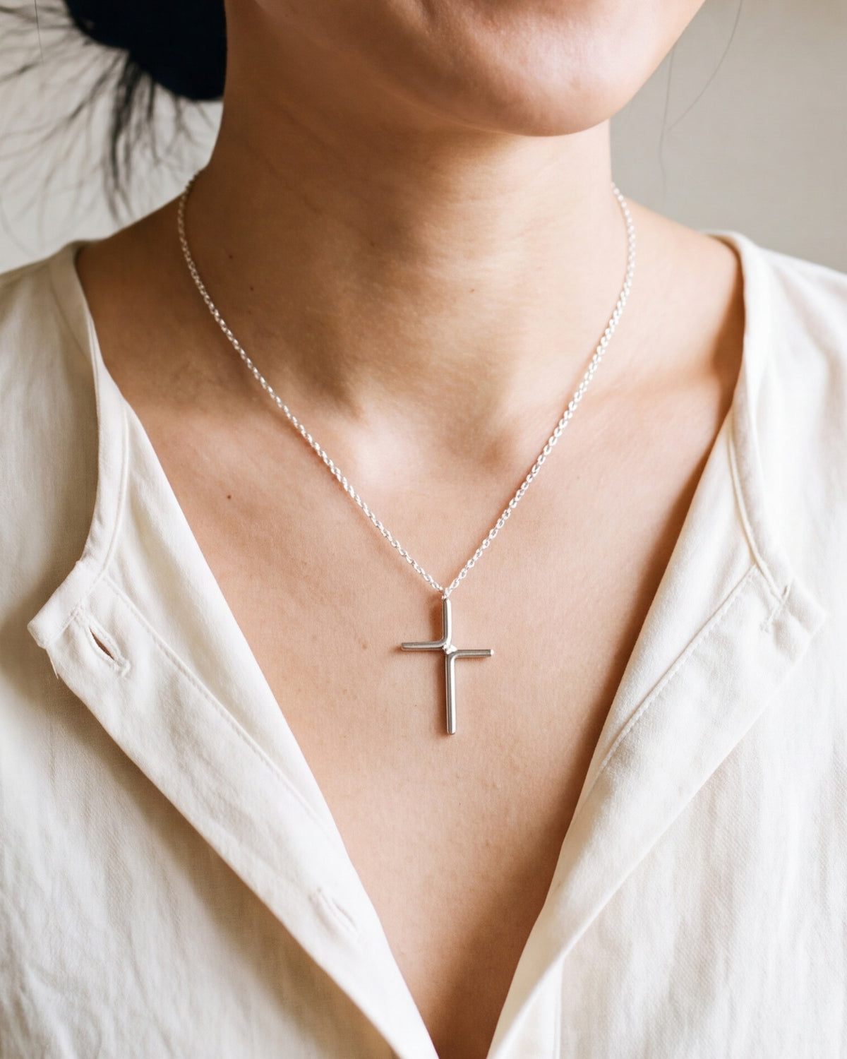 The silver Enduring Cross worn by a woman, close-up from chin to chest, true to size [c:silver]