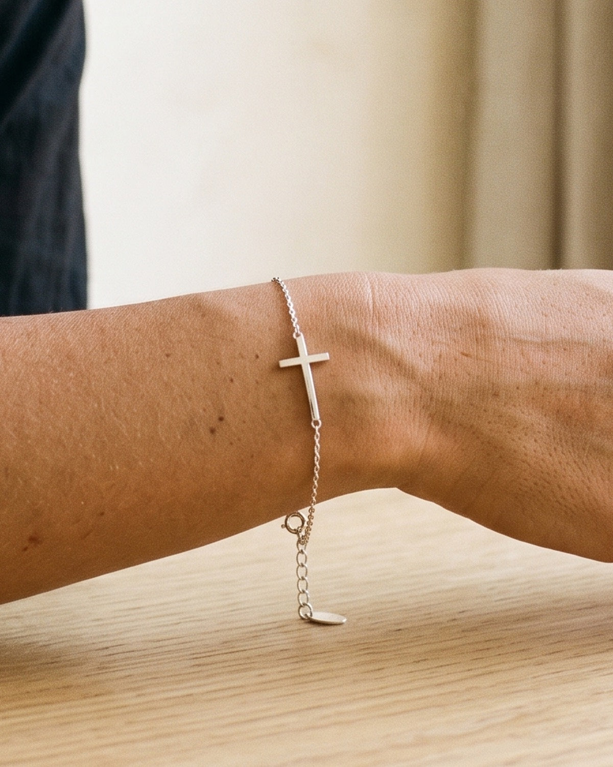 The Graceful Cross silver sideways cross bracelet on a woman's wrist, close-up, true to size