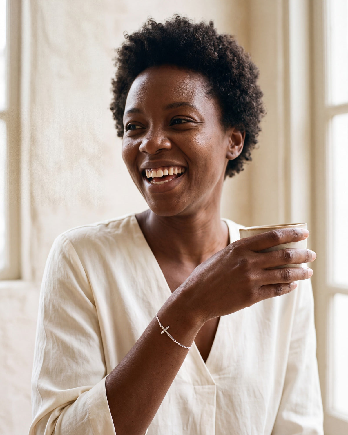 Smiling woman wearing The Graceful Cross bracelet with a cream blouse