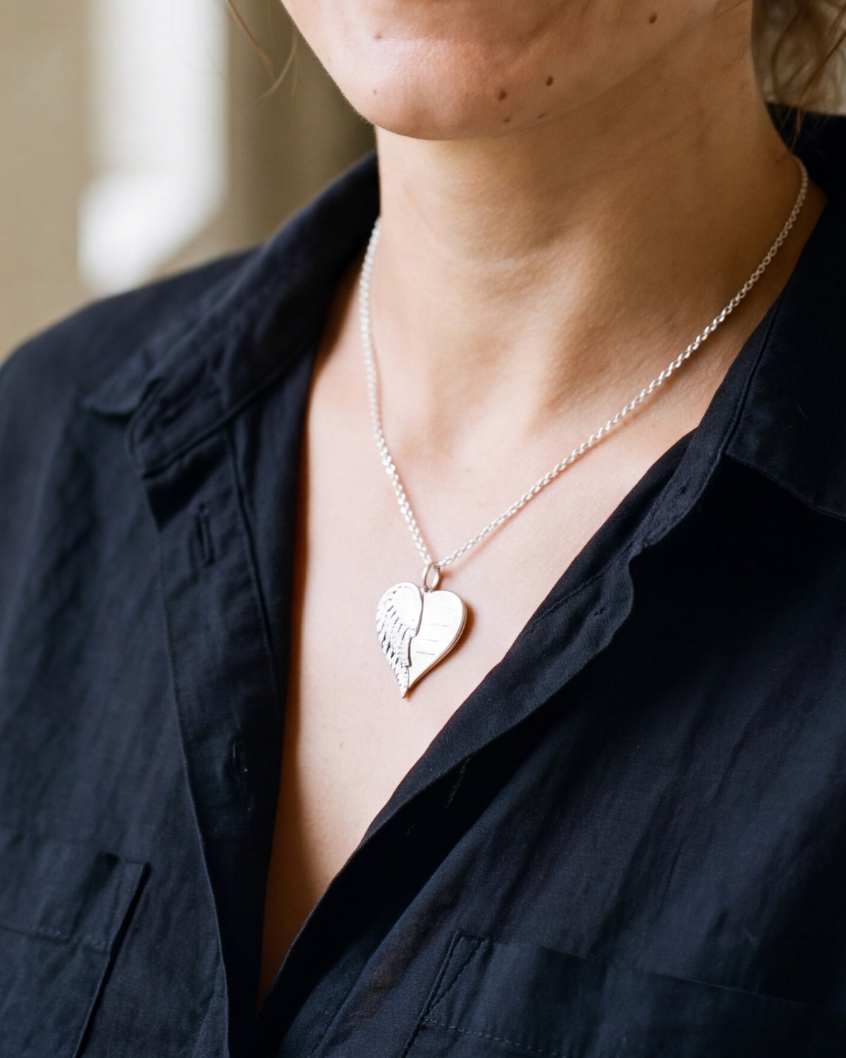 The Heart with Wings worn by a woman, close-up from chin to chest, true to size [c:silver]
