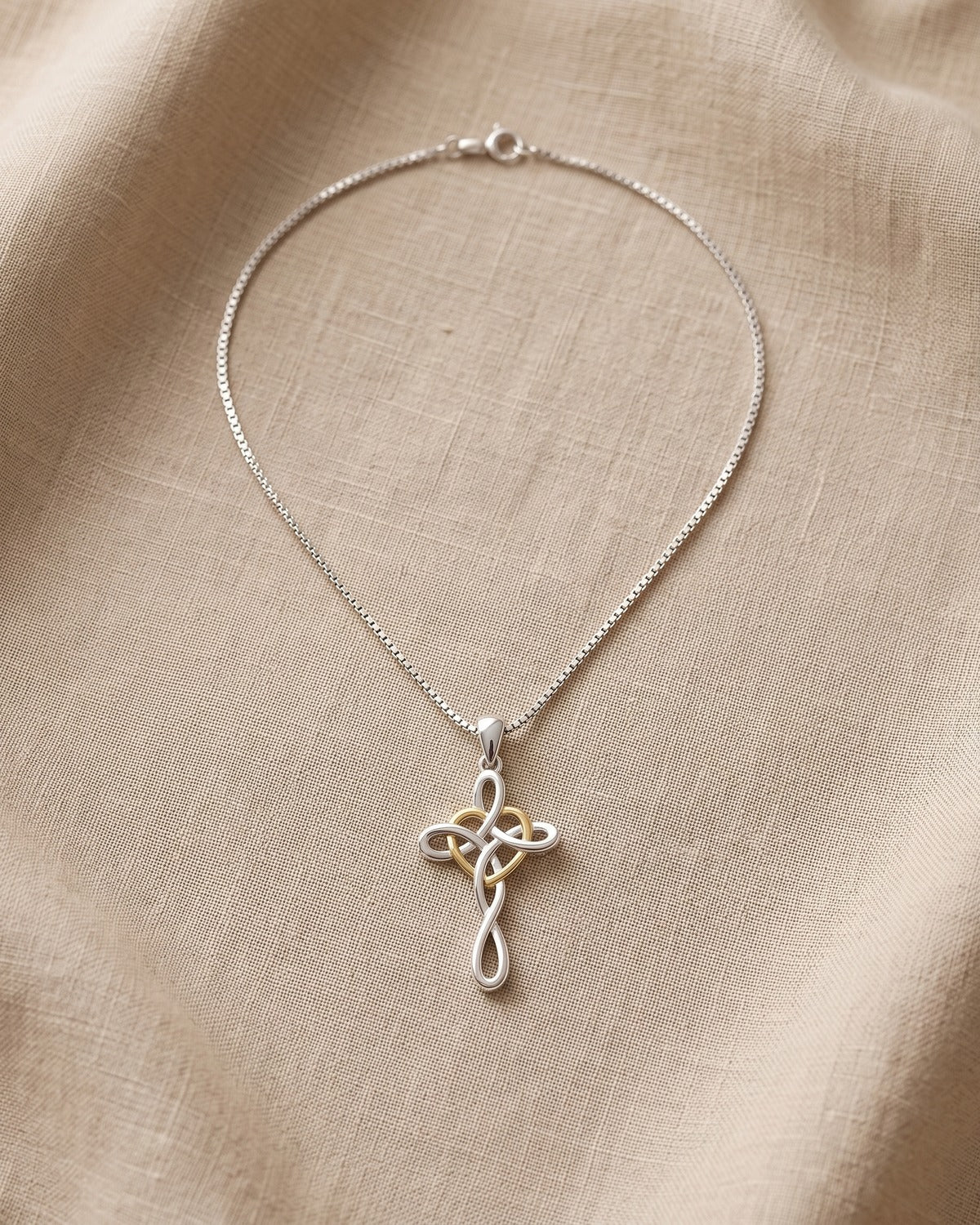 The Knotted Heart Cross necklace laid flat on linen, whole chain