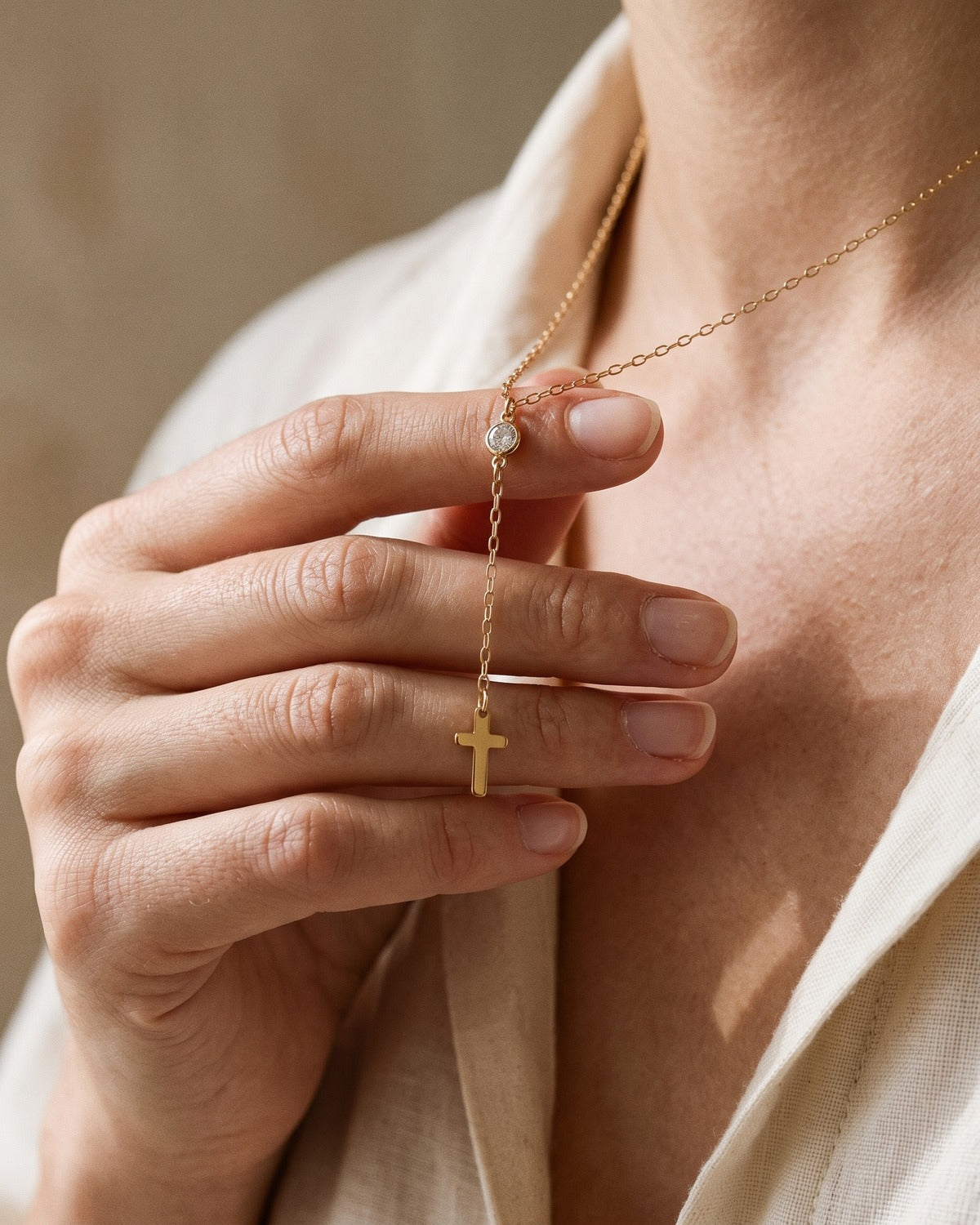 The Lariat Cross necklace held in the hand, true to size