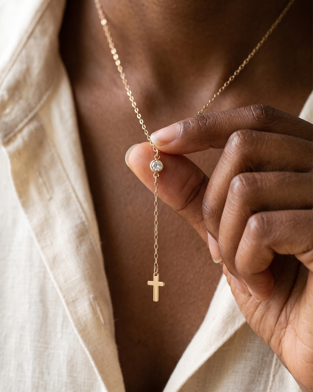 The Lariat Cross necklace held in the hand, second view, true to size