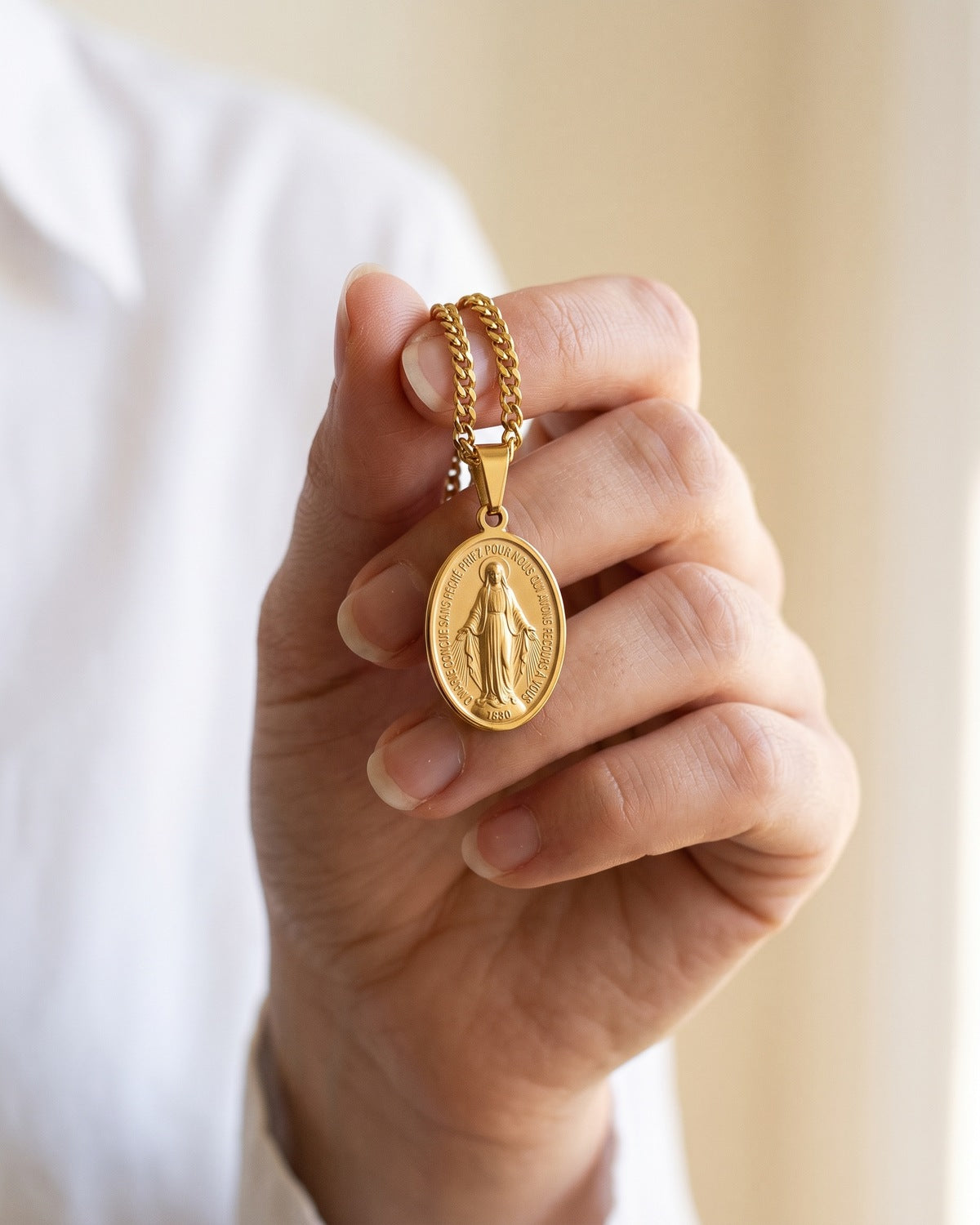 The gold Miraculous Medal held in the hand, true to size