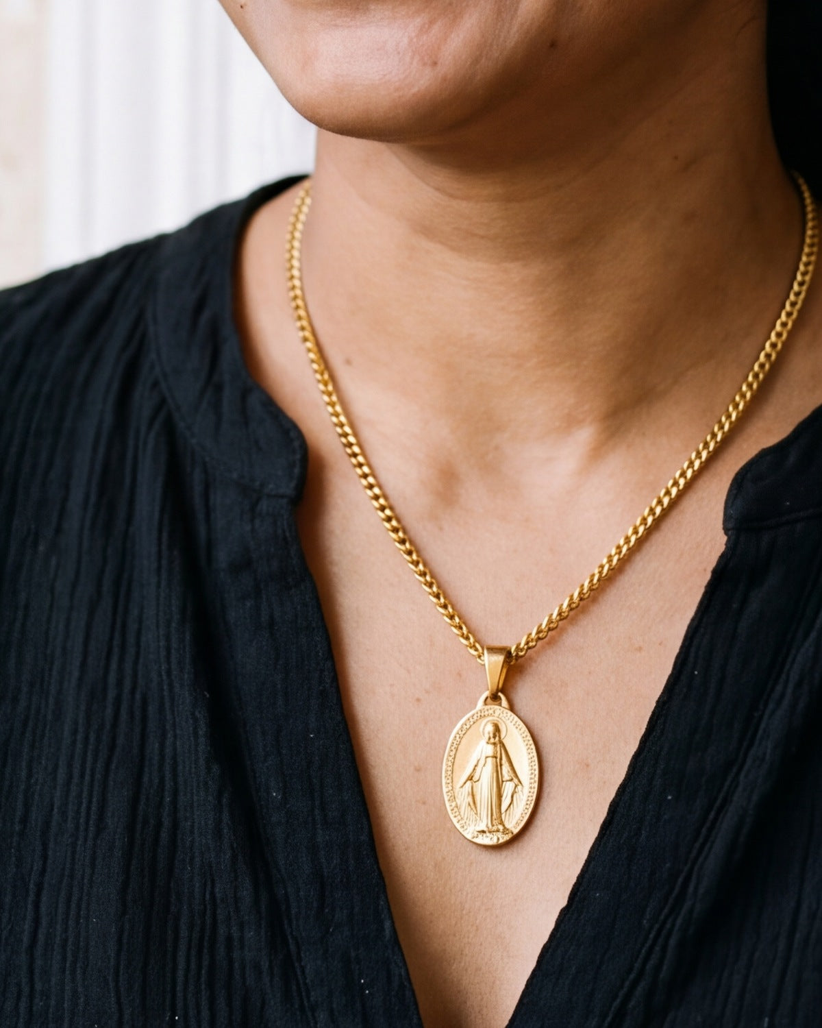 The gold Miraculous Medal worn by a woman, close-up from chin to chest, true to size