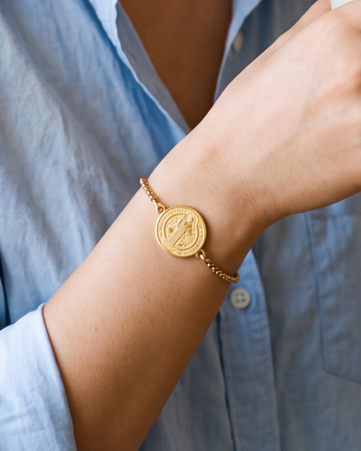 The gold Sacred Medal Bracelet worn by a woman, close-up, true to size