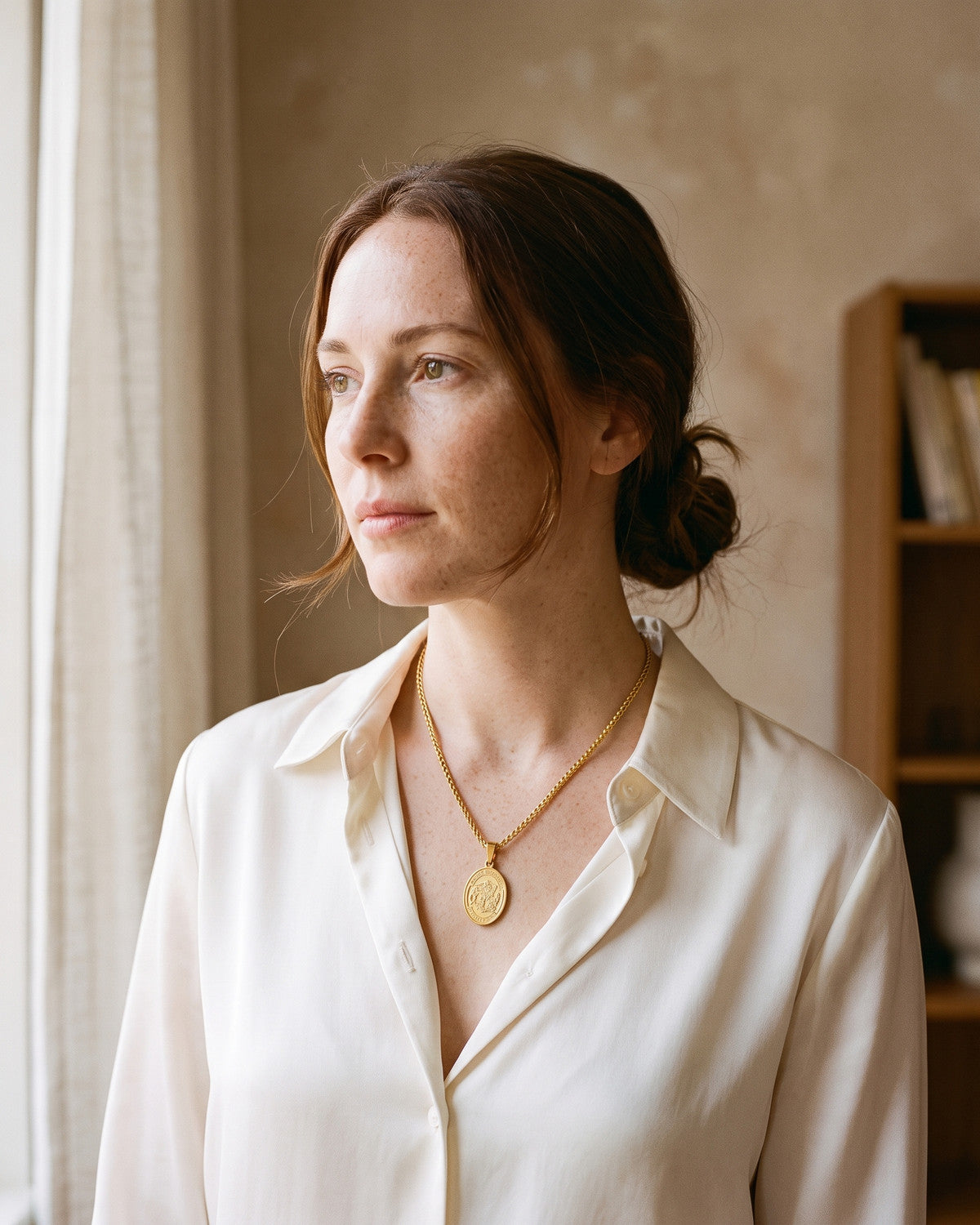 Woman wearing the gold Saint Michael Medal with a silk blouse