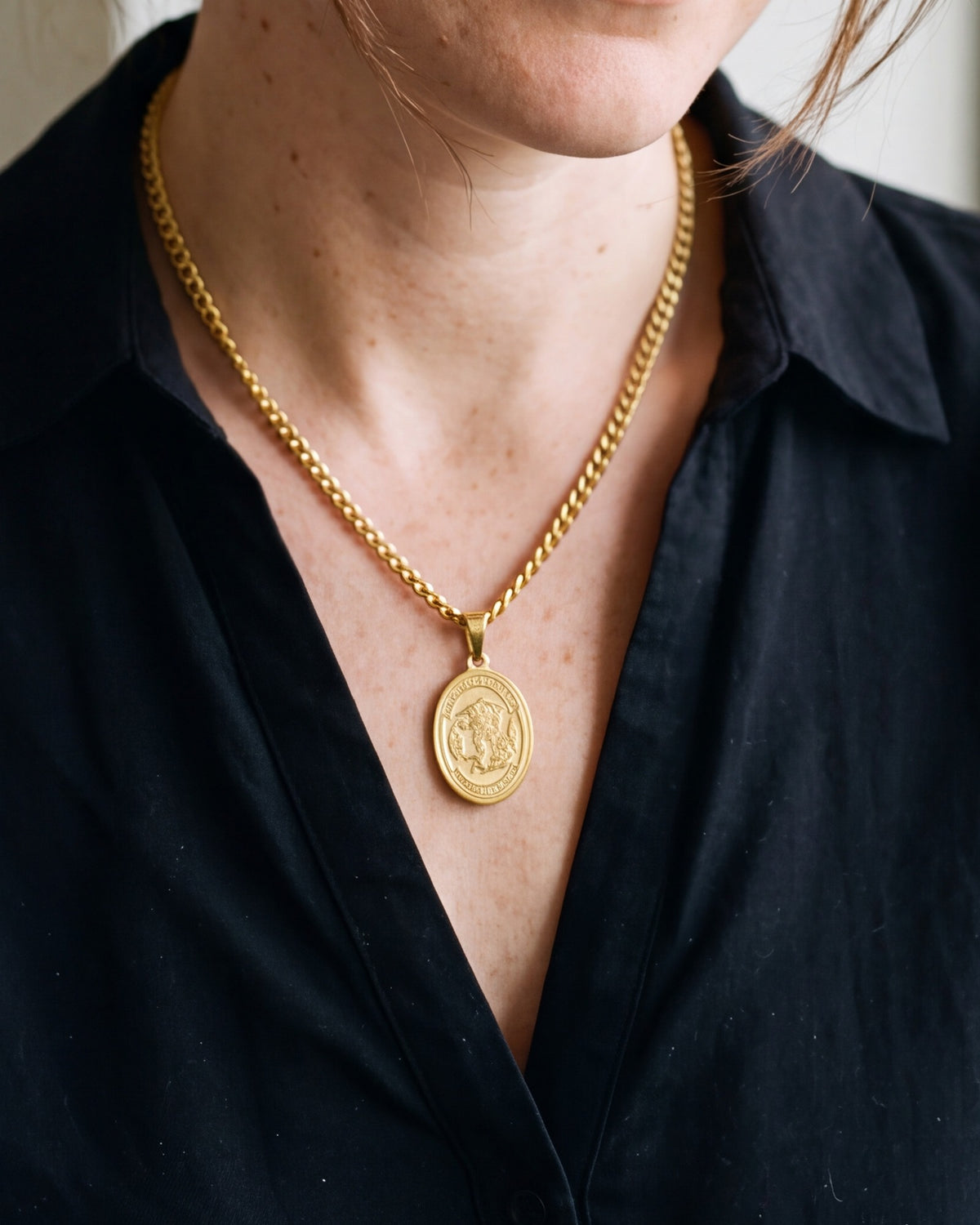 The gold Saint Michael Medal worn by a woman with a black blouse, close-up, true to size [c:gold]