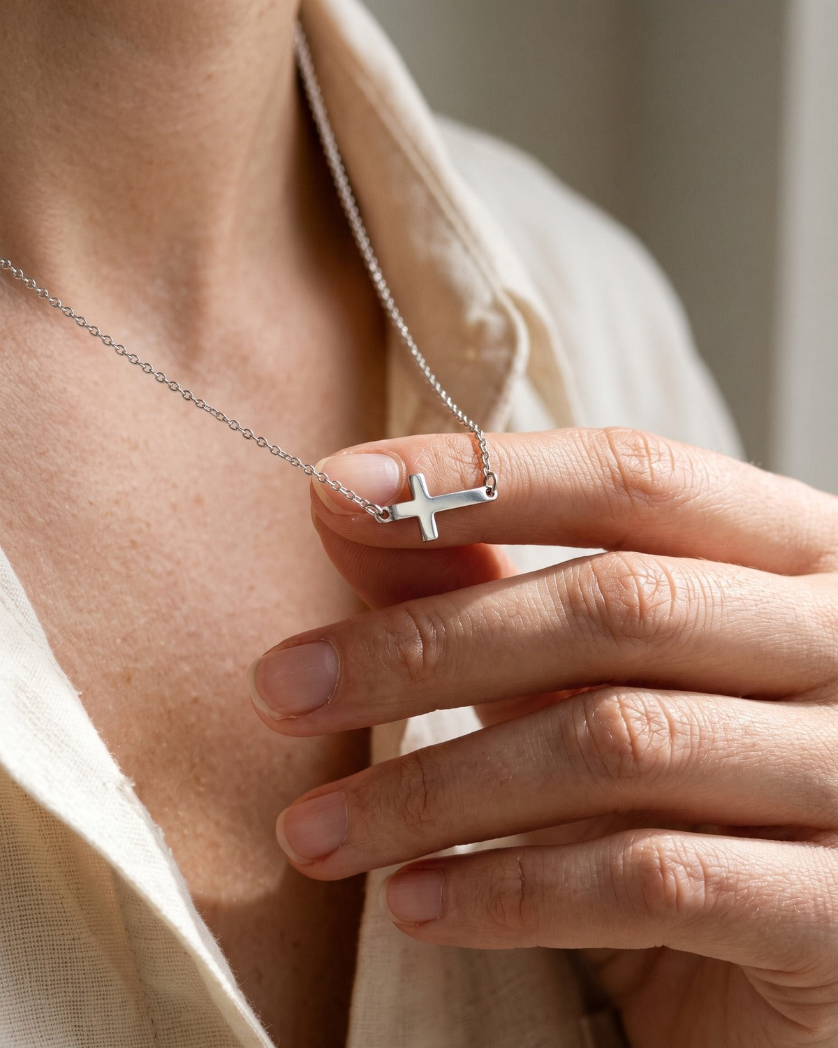 The Sideways Cross necklace held in the hand, true to size [c:silver]