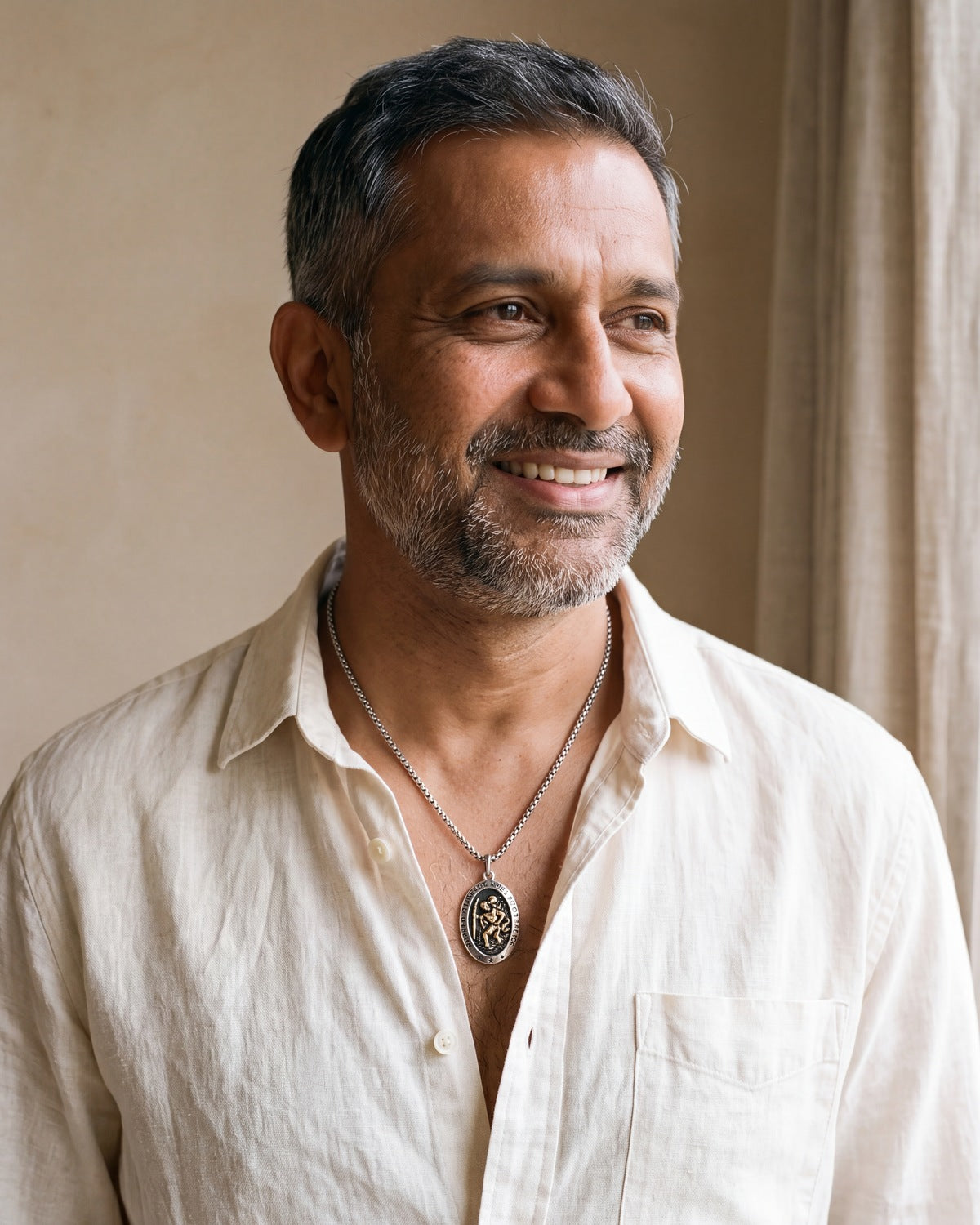 Smiling man wearing The Voyager's Protector Saint Christopher necklace with a linen shirt